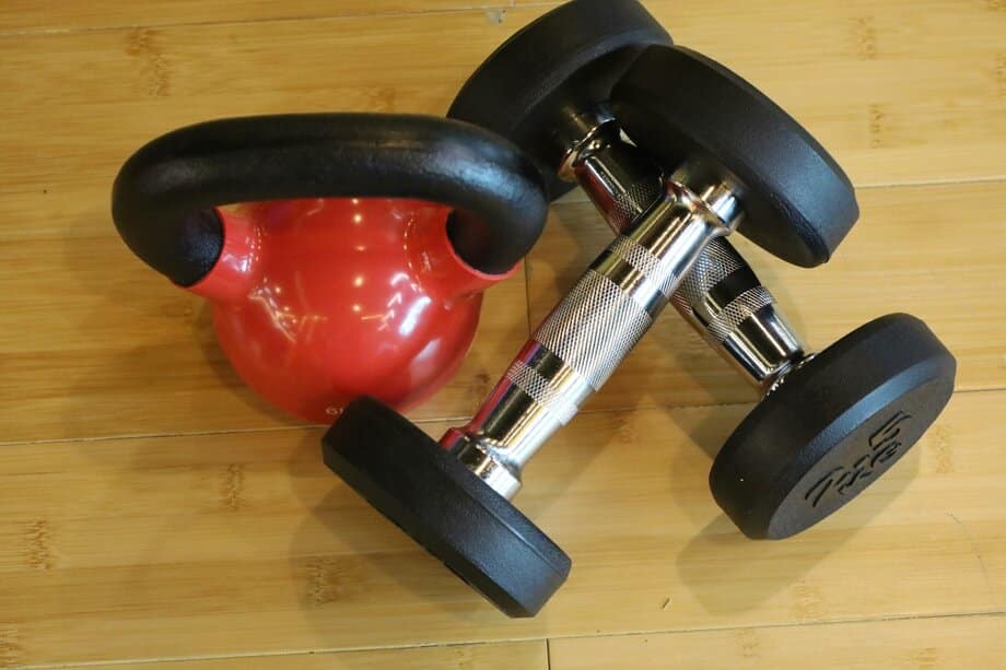 Vergelijking dumbbells en kettlebell op een parketvloer thuis — voor- en nadelen zichtbaar